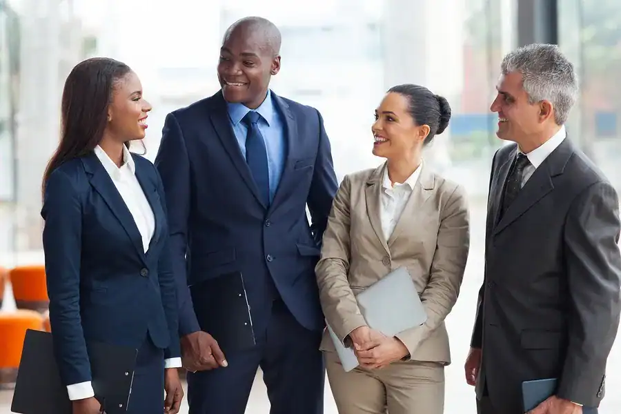 Four professionals in business attire holding folders and laptops engage in conversation at a corporate event.